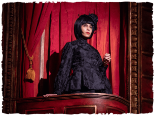 woman wearing black in a booth with a red curtain