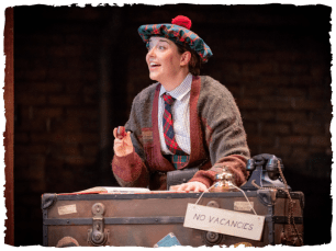 Performer in a scottish bonnet stands over a suitcase