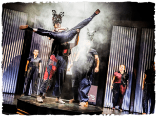 A performer is hoisted into the air by another as others look on and there is smoke in the air