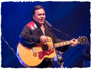 Sweet caroline production image - man dressed as Neil Diamon holding a guitar
