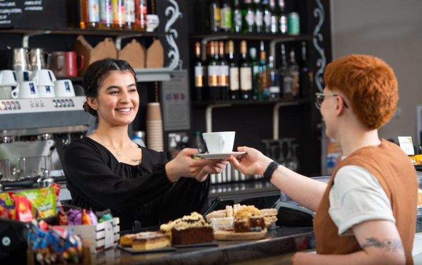 A cafe assistant handing a coffee to a customer