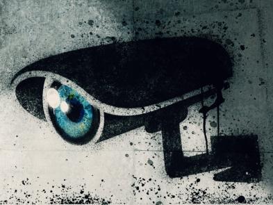 A grey brick wall with a spray painted image of a security camera