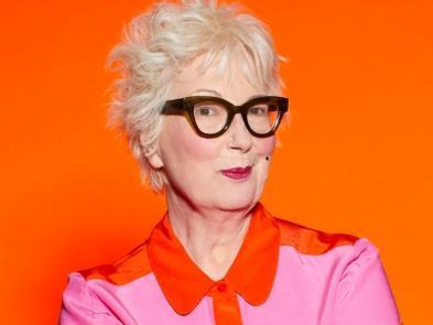 Jenny Eclair on an orange background wearing a pink top 