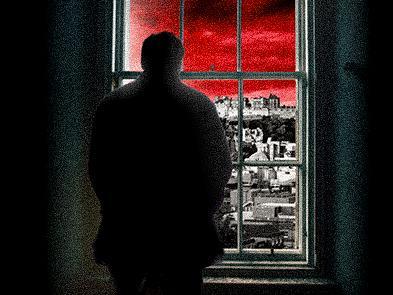 A man stands by a window looking out at a city with a red sky