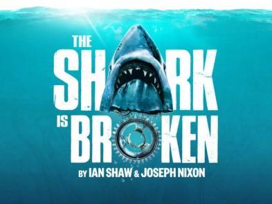 The Shark is Broken in white text with a Sharks Head placed to represent the A and a giant cog to represent the O, all are under the ocean