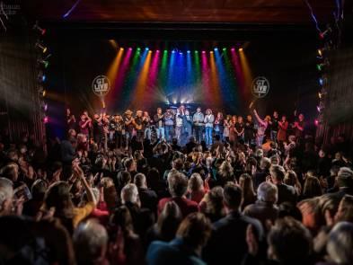 Image of crowd in front of Yvonne Arnaud stage, at the end of a concert, with the artists and musicians on stage taking a bow.