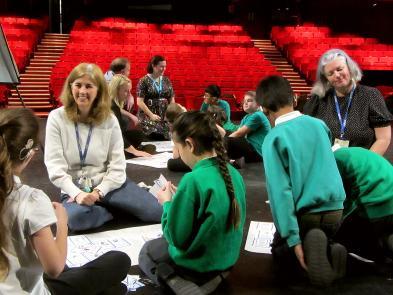 A group of school children engaged in an activity on stage of the theatre.