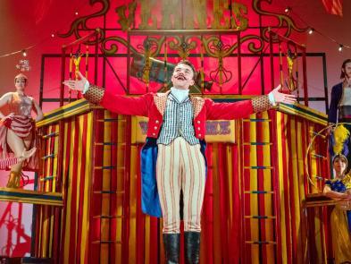 Performer raising his cane and arms with a circus background